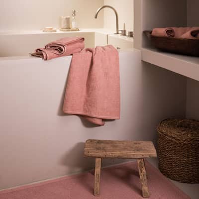 Linge de bain rose dans une salle de bain chaleureuse avec baignoire et panier en osier