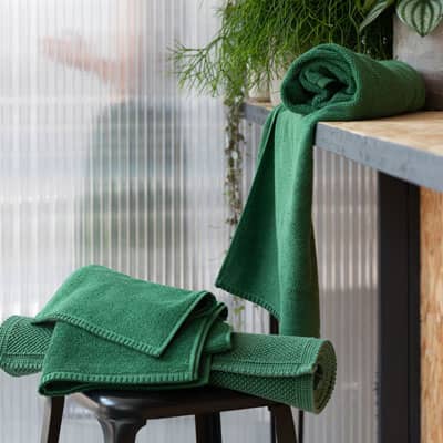 Serviettes en coton vert pliées et suspendues dans une salle de bain avec plante