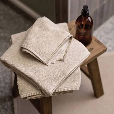 Serviettes en éponge de coton beige pliées sur un tabouret en bois dans une salle de bain